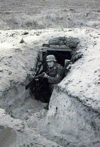 Een Duitse soldaat met geweer in de aanslag uit een bunker. De betreffende bunker stond in de duinen bij de Bure Blinkert. (foto 15 september 1943)