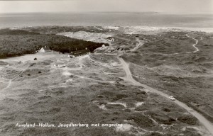 Een ansichtkaart met daarop de Jeugdherberg van de NJHC. Deze werd gevestigd in het voormalig hoofdkwartier van de Kriegsmarine gelegen aan het einde van de Oranjeweg te Hollum. De op de foot niet zichtbare bunkers werden gebruikt als slaapzalen. Deze zijn inmiddels vervangen door nieuwbouw. Alle op de kaart zichtbare gebouwen waren onderdeel van het Hoofdkwartier. Rechts van de gebouwen zien we boben op het duin de funderingen van de Flakstelling. (foto 29 juni 1950)