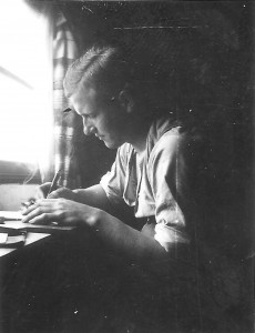 Jonge Duitse soldaat zit in zijn verblijf aan tafel te schrijven, foto genomen tijdens het eerste jaar van de oorlog. (15 oktober 1940)